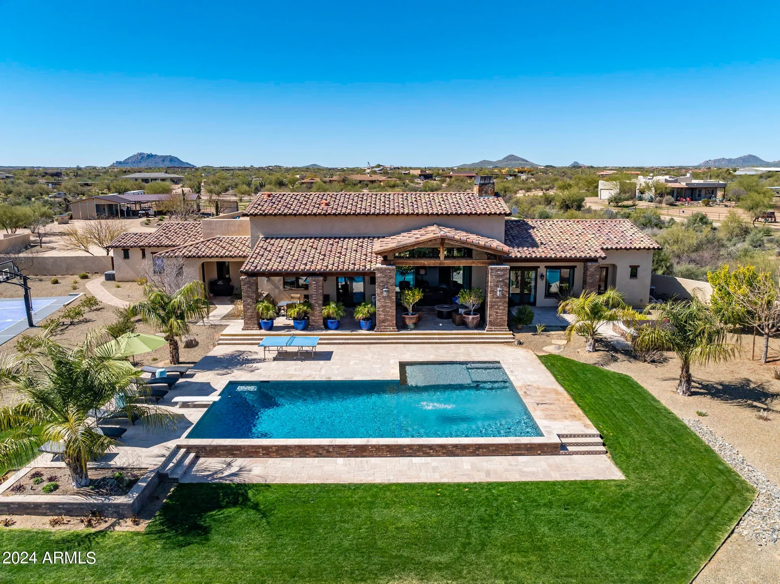 Aerial view of a desert residence with a swimming pool, landscaped grounds, and sports court