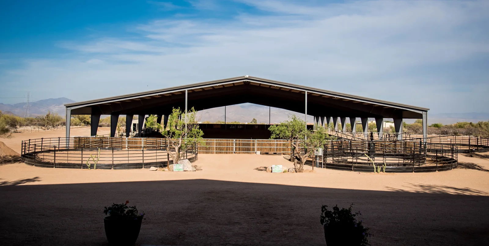 Covered equestrian riding arena with outdoor paddocks in a desert setting