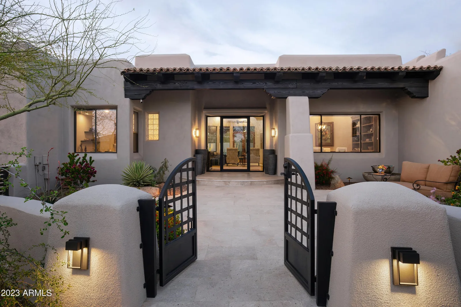 Desert home entrance framed by stucco walls and an open gate at dusk