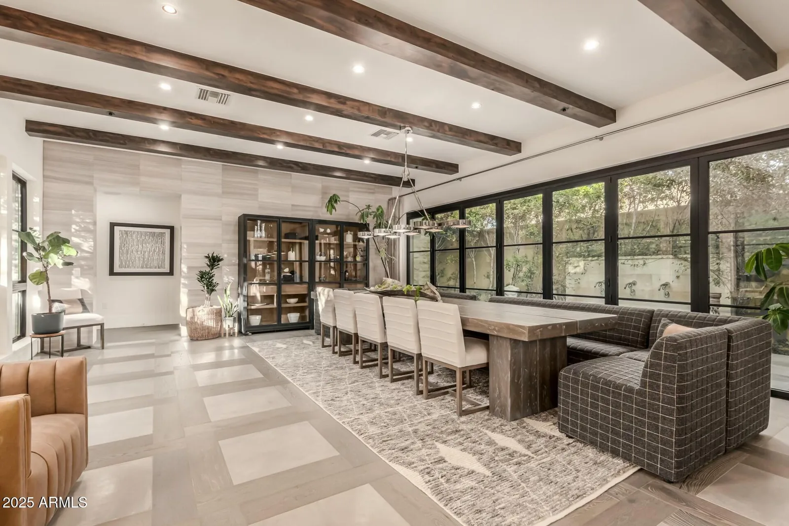 Dining area with a long table and window wall beneath exposed wood beams