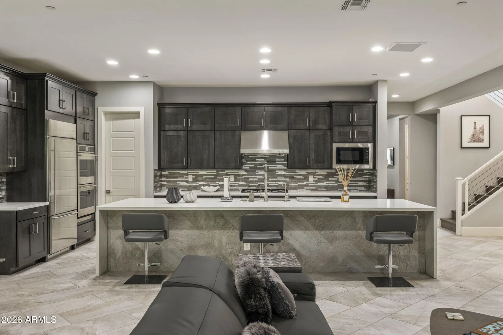 Kitchen and living room with dark cabinetry, a stone island, and a staircase