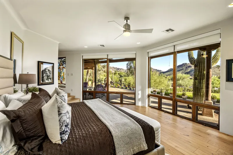 Primary bedroom with wood floors, a ceiling fan and glass doors opening to a desert garden and mountain view