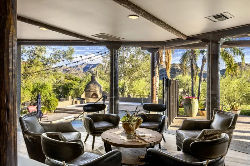 Covered outdoor lounge with leather chairs, a stone fireplace and mountain views beyond the patio
