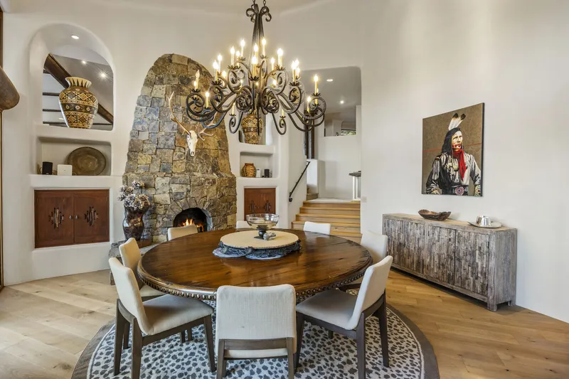 Dining room with a round wood table, chandelier and a stone fireplace in an arched alcove