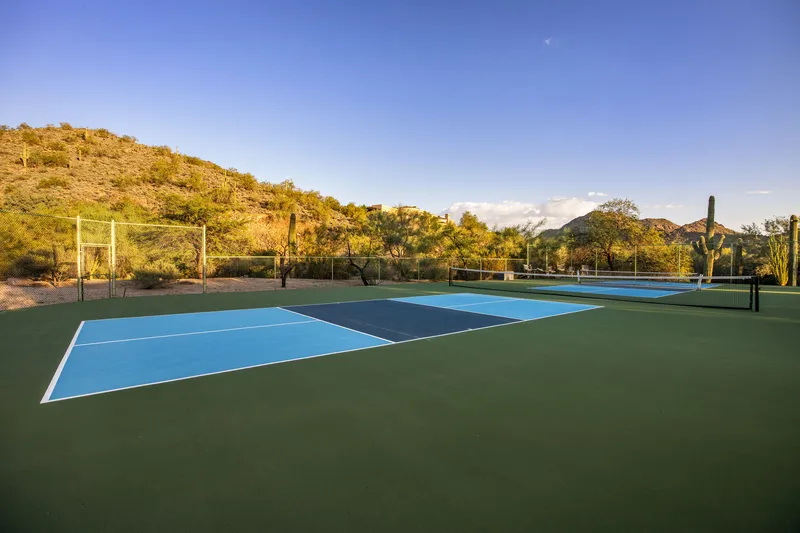 Pickleball court with blue and green surface and a hillside beyond the fence at golden hour
