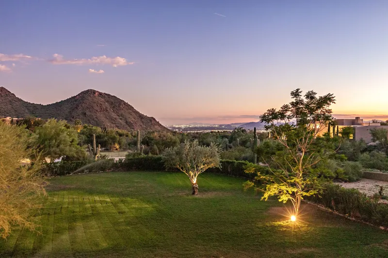 Manicured lawn with an uplit tree and a desert mountain silhouetted against a sunset sky